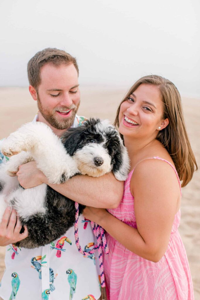 Portrait of smiling couple holding adorable puppy at the beach, professional lifestyle photography.