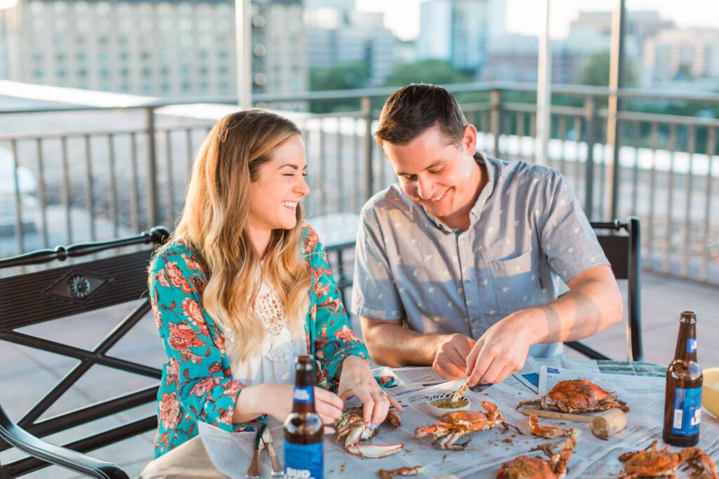 Romantic outdoor rooftop dining with seafood, drinks, city skyline in background.