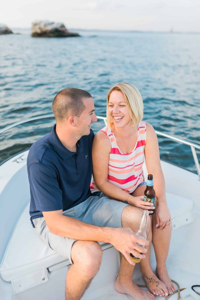 Relaxed couple smiling and laughing on a boat with drinks, capturing joyful romantic moments outdoors, pristine water background.