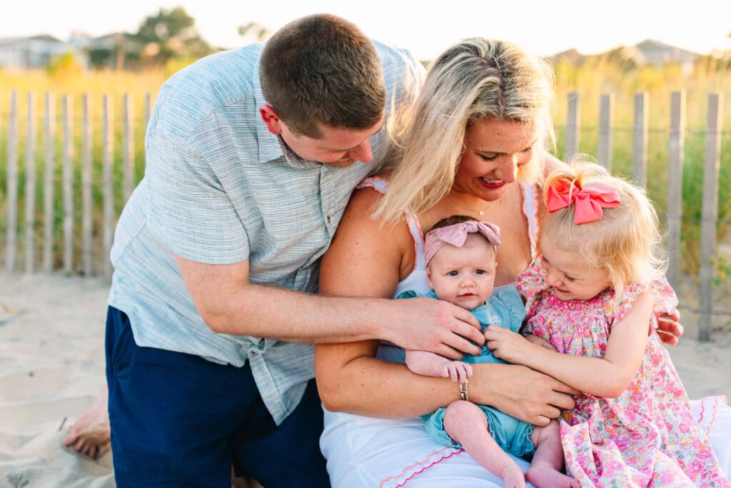 Family enjoying tender moment at the beach, vibrant sunset lighting in the background.