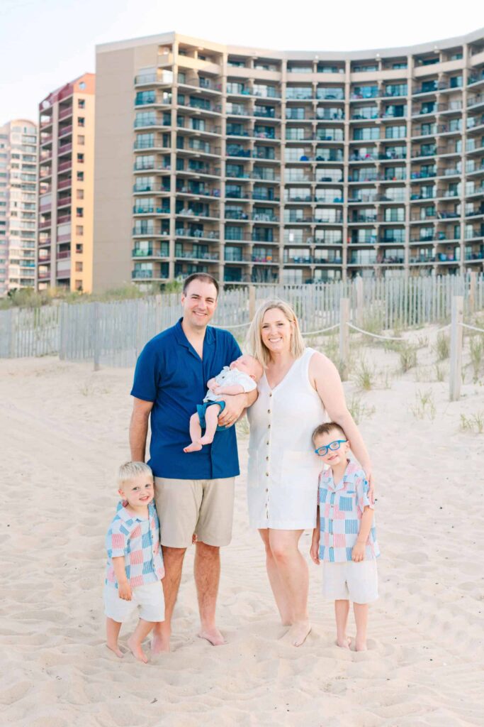 Bright family portrait on the beach with kids, parents, and urban buildings behind.